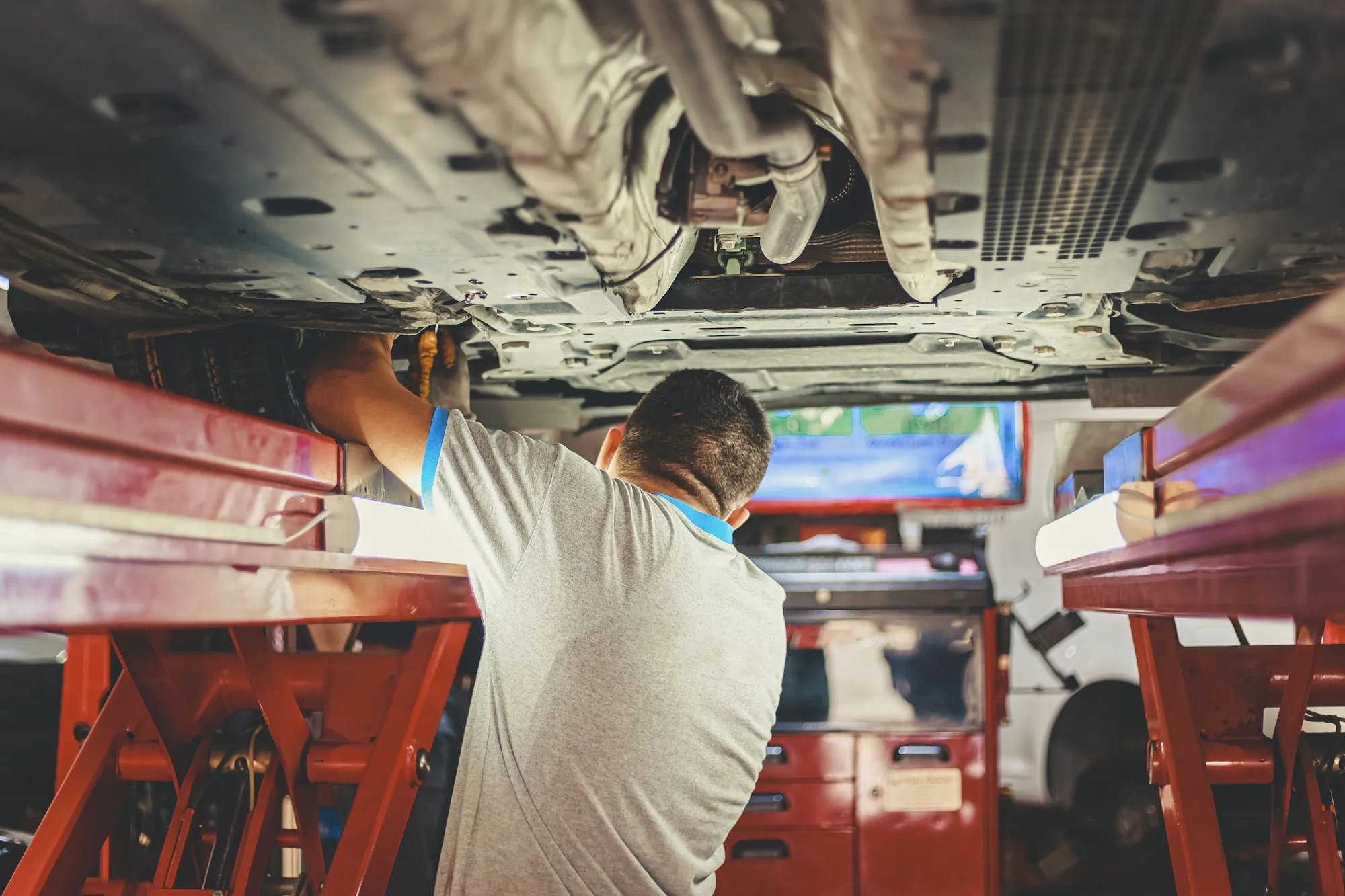 Mechanic working on the underside of a car raised on a red lift